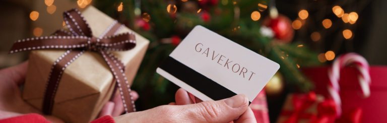 Gavekort i Oslo, bilde av en hånd som holder et gavekort foran en gave og et juletre